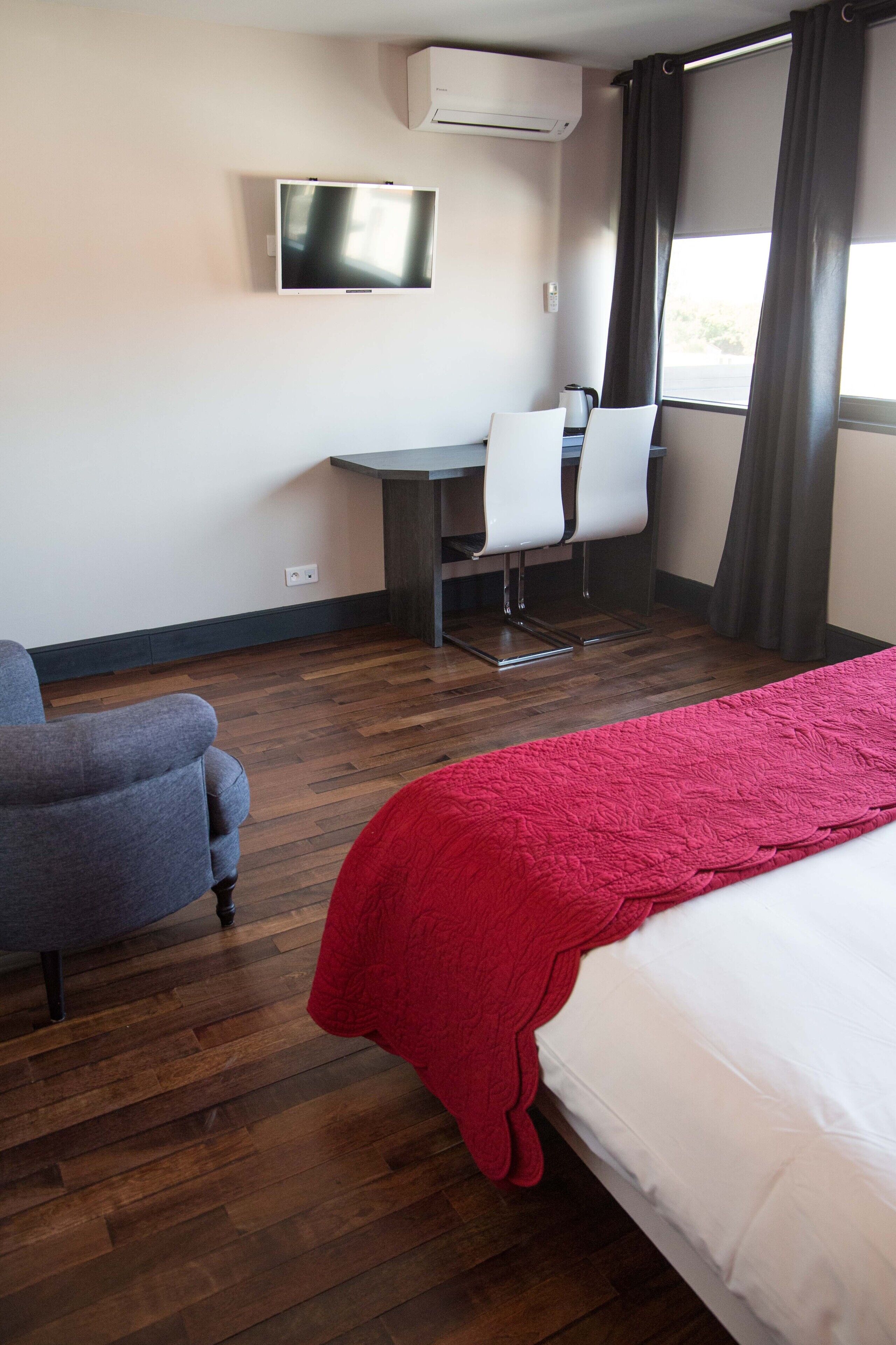 Een hotelkamer met een bed, een bureau met twee stoelen, een televisie en een raam met gordijnen.