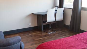 Een hotelkamer met een bed, een bureau met twee stoelen, een televisie en een raam met gordijnen.