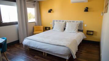 A bedroom with a large bed, a small table, a chair, and a window with curtains.