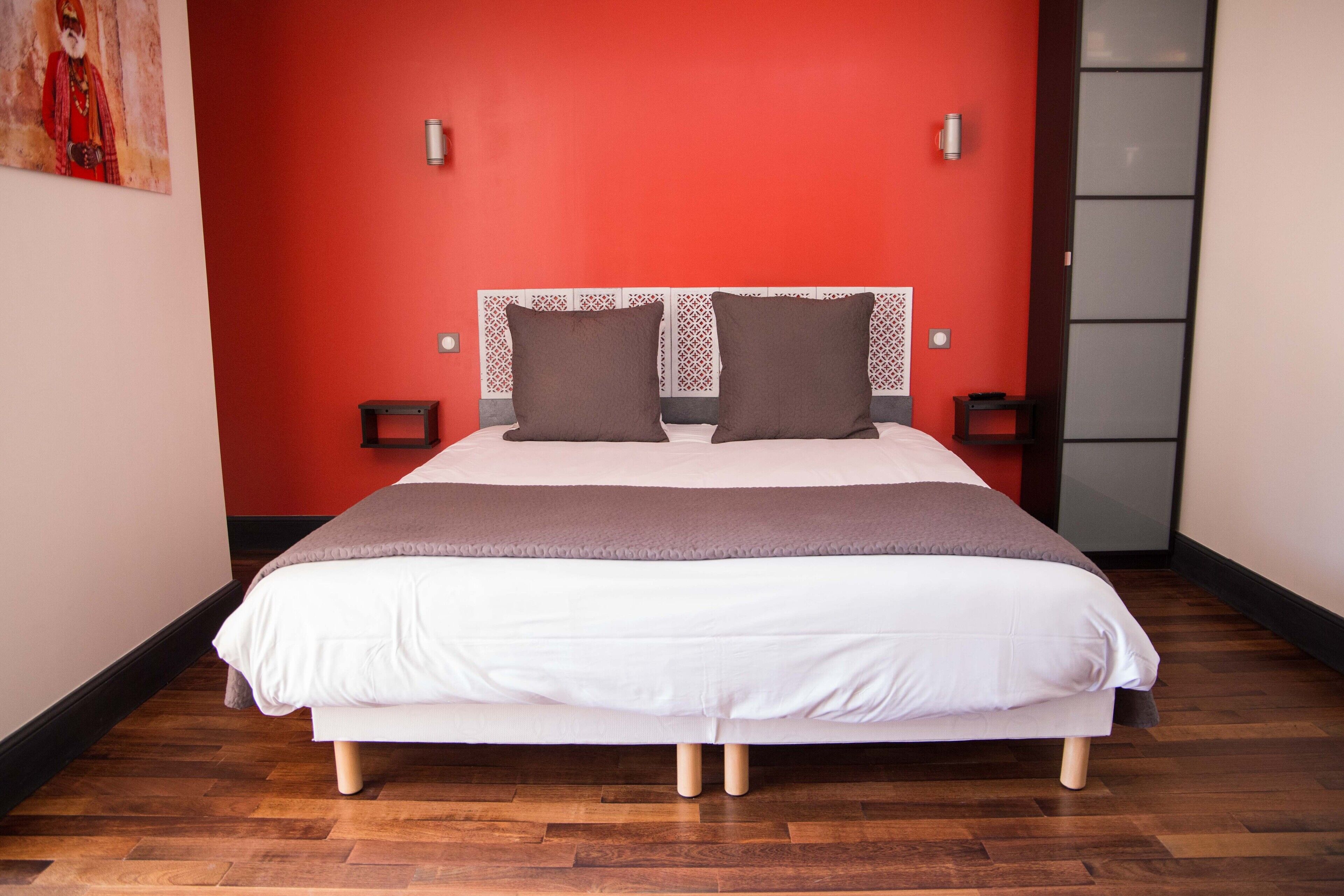 A neatly made bed with a white and brown color scheme, positioned against a red wall with a decorative headboard.