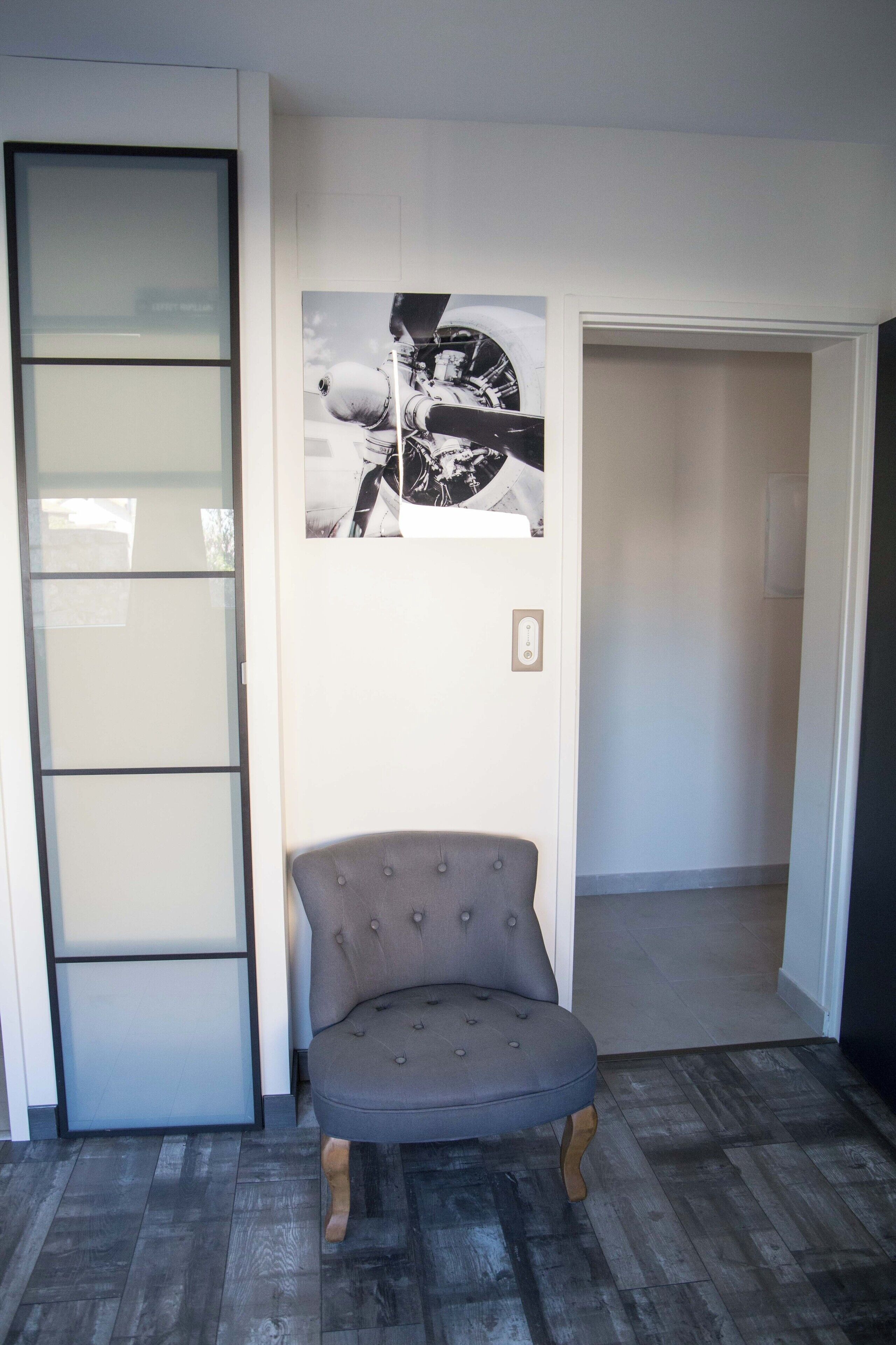 A room with a grey upholstered armchair, a black and white photograph on the wall, and a sliding glass door.