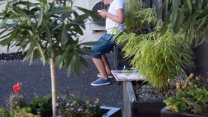 A person sitting on a bench in an outdoor area with potted plants and a building in the background. - Appart hôtel Chanzy Angoulême Soyaux (Soyaux)