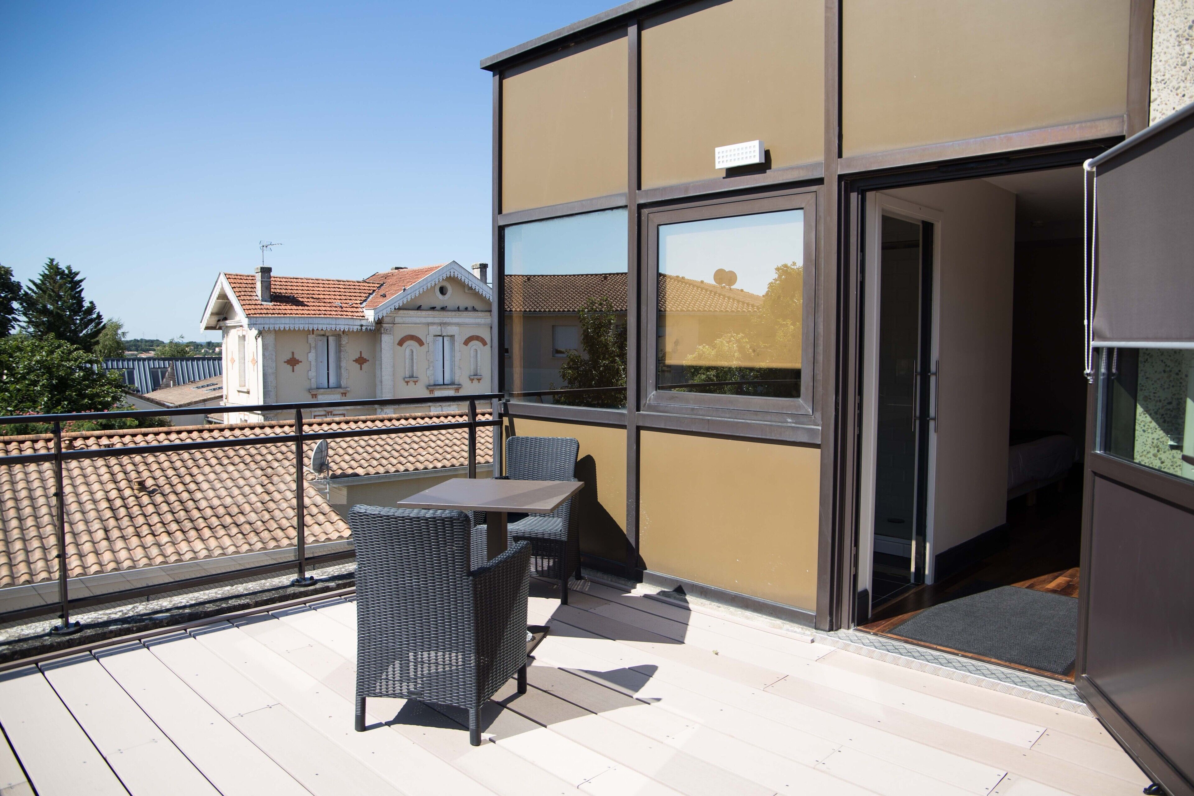 A balcony with outdoor furniture, a clear view of the neighboring buildings, and a door leading to an interior space.