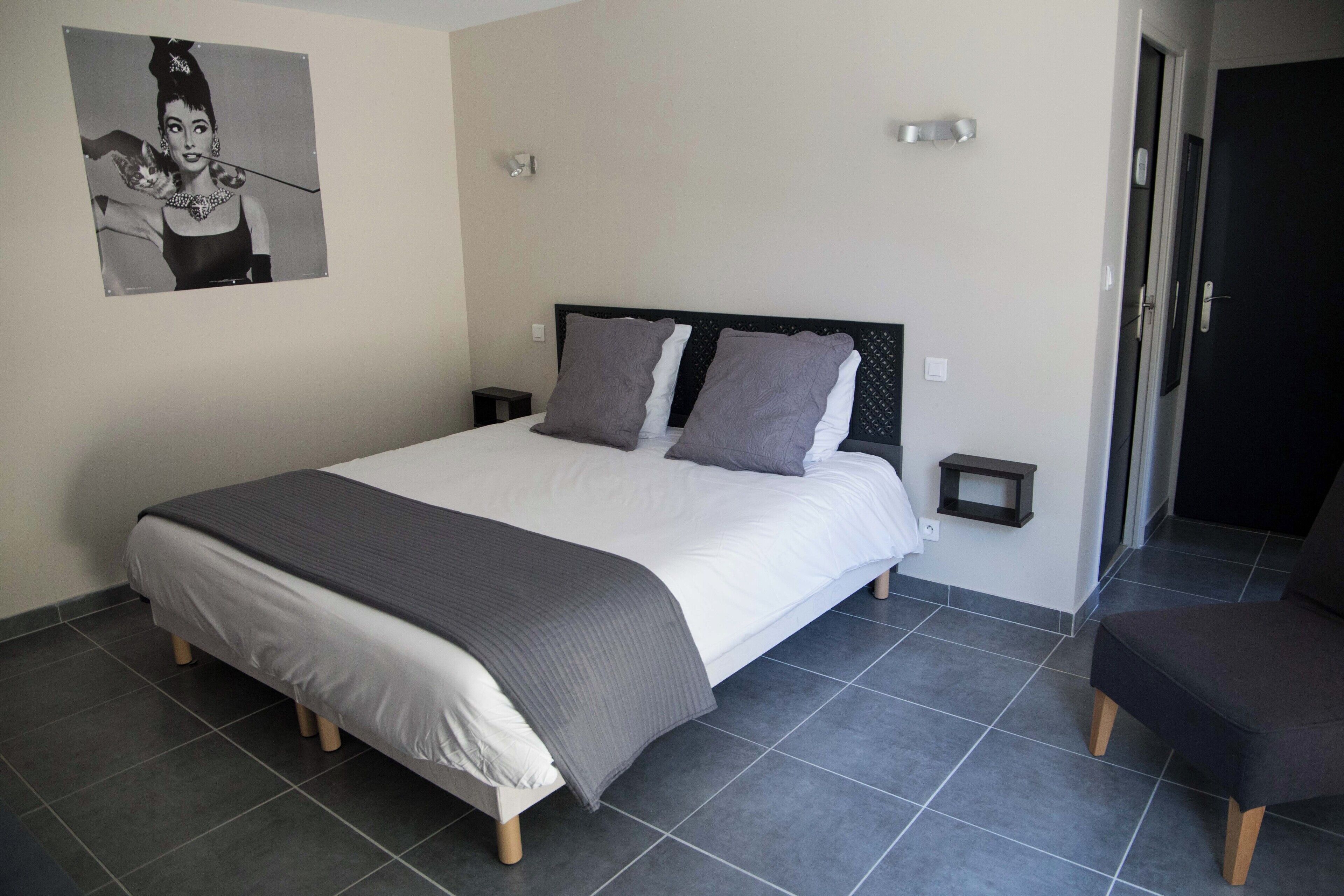 A bedroom with a bed, two bedside tables, a chair, a wall-mounted picture, and a door.