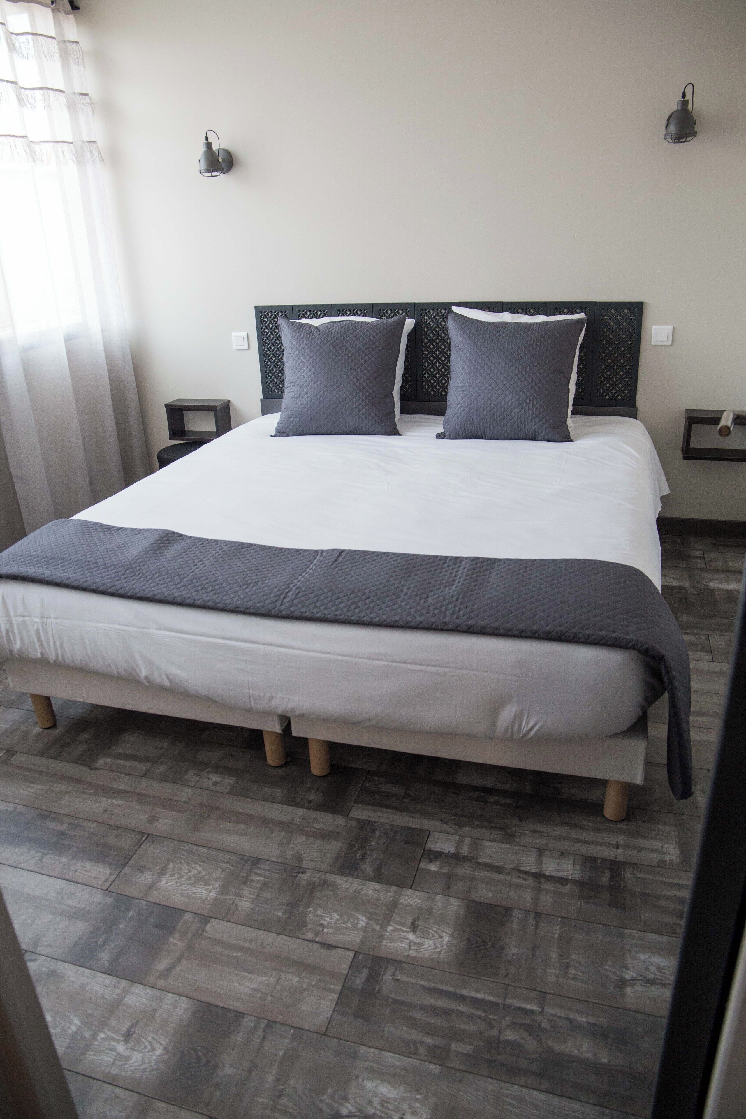 A neatly made bed with a grey blanket and pillows, a wooden headboard, and a bedside table with a lamp.