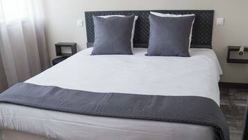 A neatly made bed with a grey blanket and pillows, a wooden headboard, and a bedside table with a lamp.