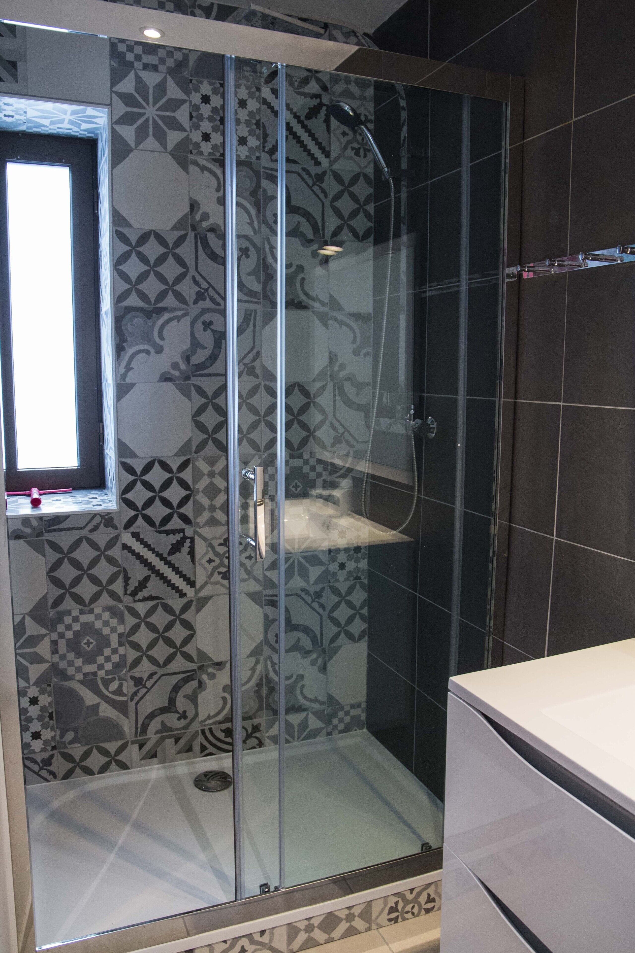 A shower with a glass door, patterned tiles, and a window.