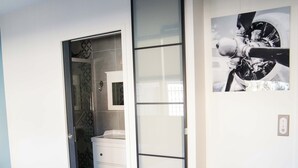 A bedroom with a bed, a grey upholstered chair, a white dresser, and a sliding door leading to a bathroom. - Appart hôtel Chanzy Angoulême Soyaux (Soyaux)