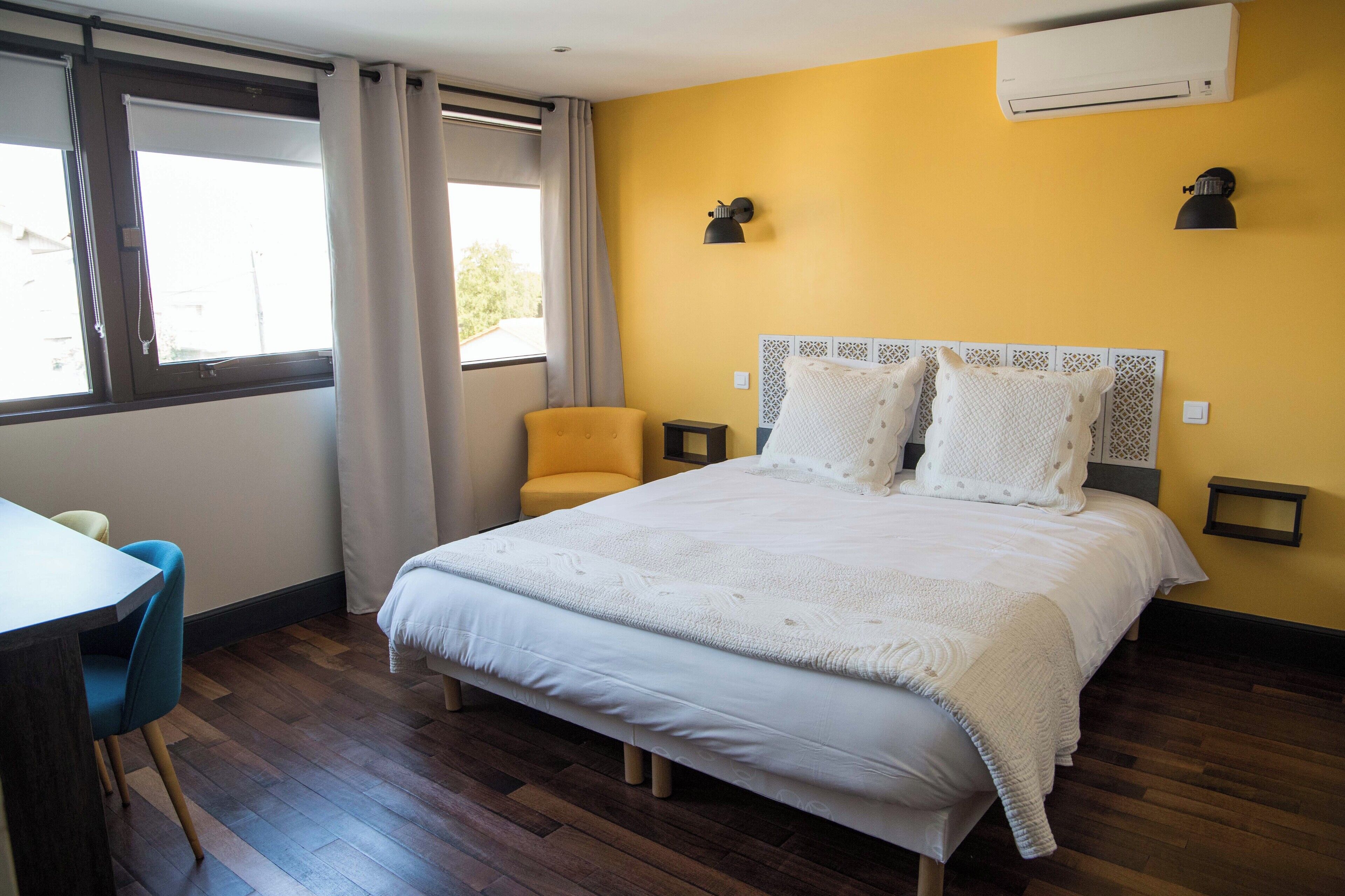 A bedroom with a bed, a chair, a desk, and an air conditioning unit.