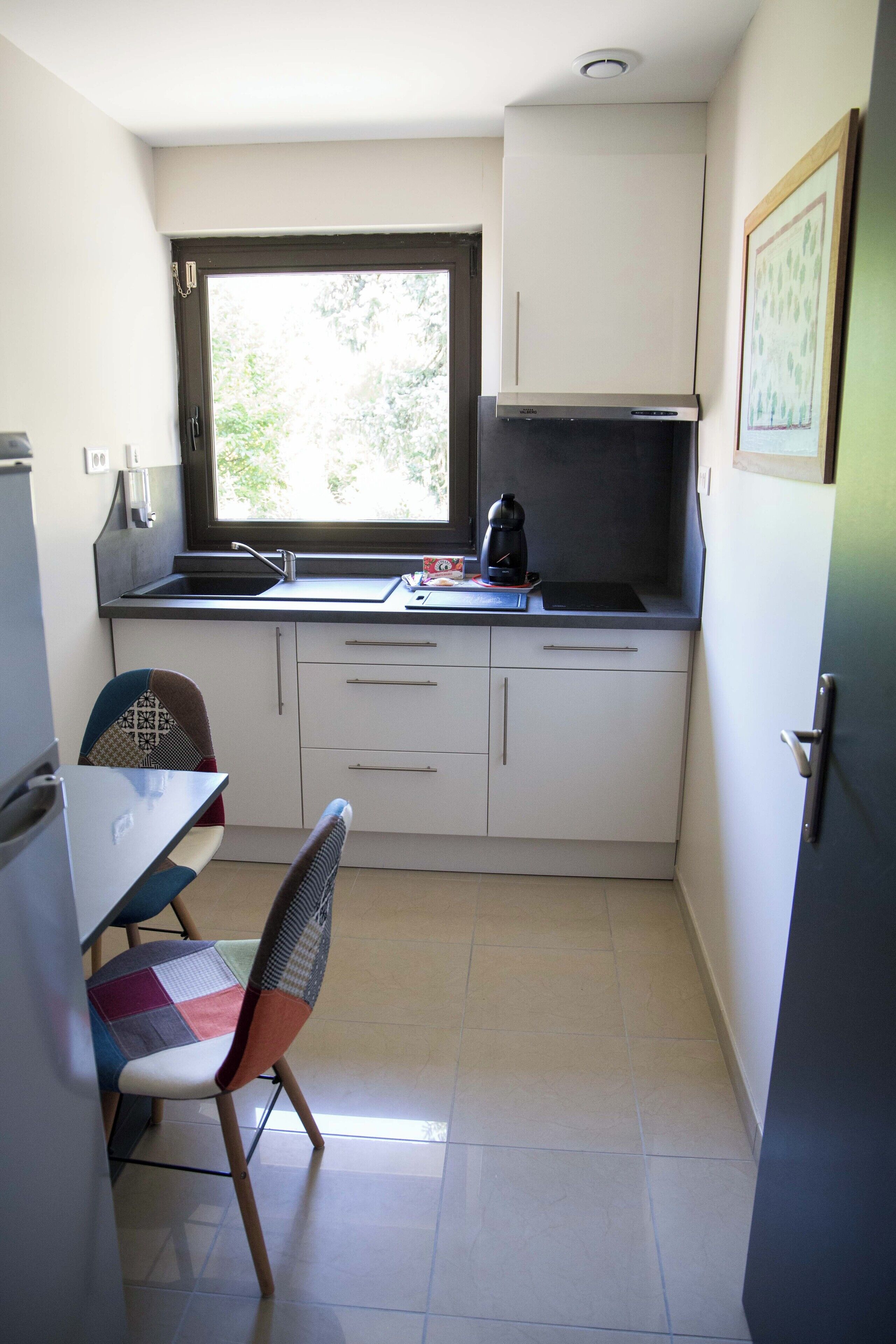 Une petite cuisine équipée d’une fenêtre, d’un évier, d’une cuisinière et d’une chaise.