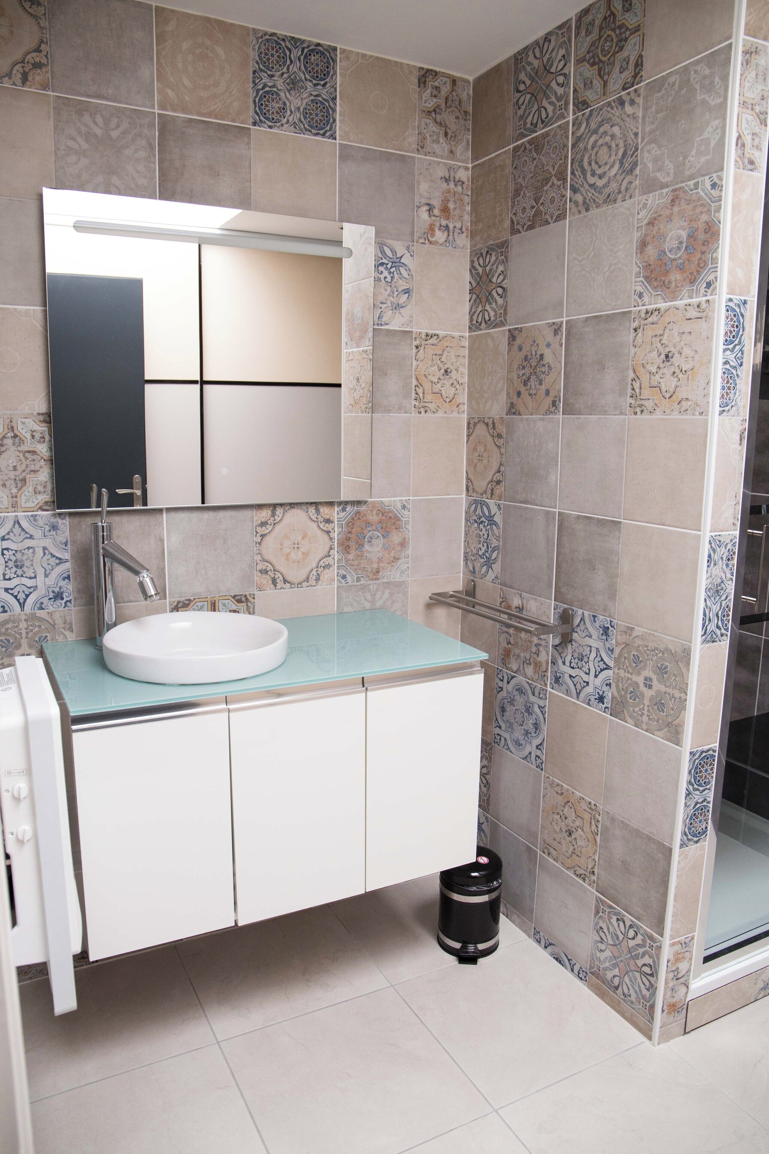 A bathroom with a white sink, a mirror, and patterned tiles on the walls and floor.