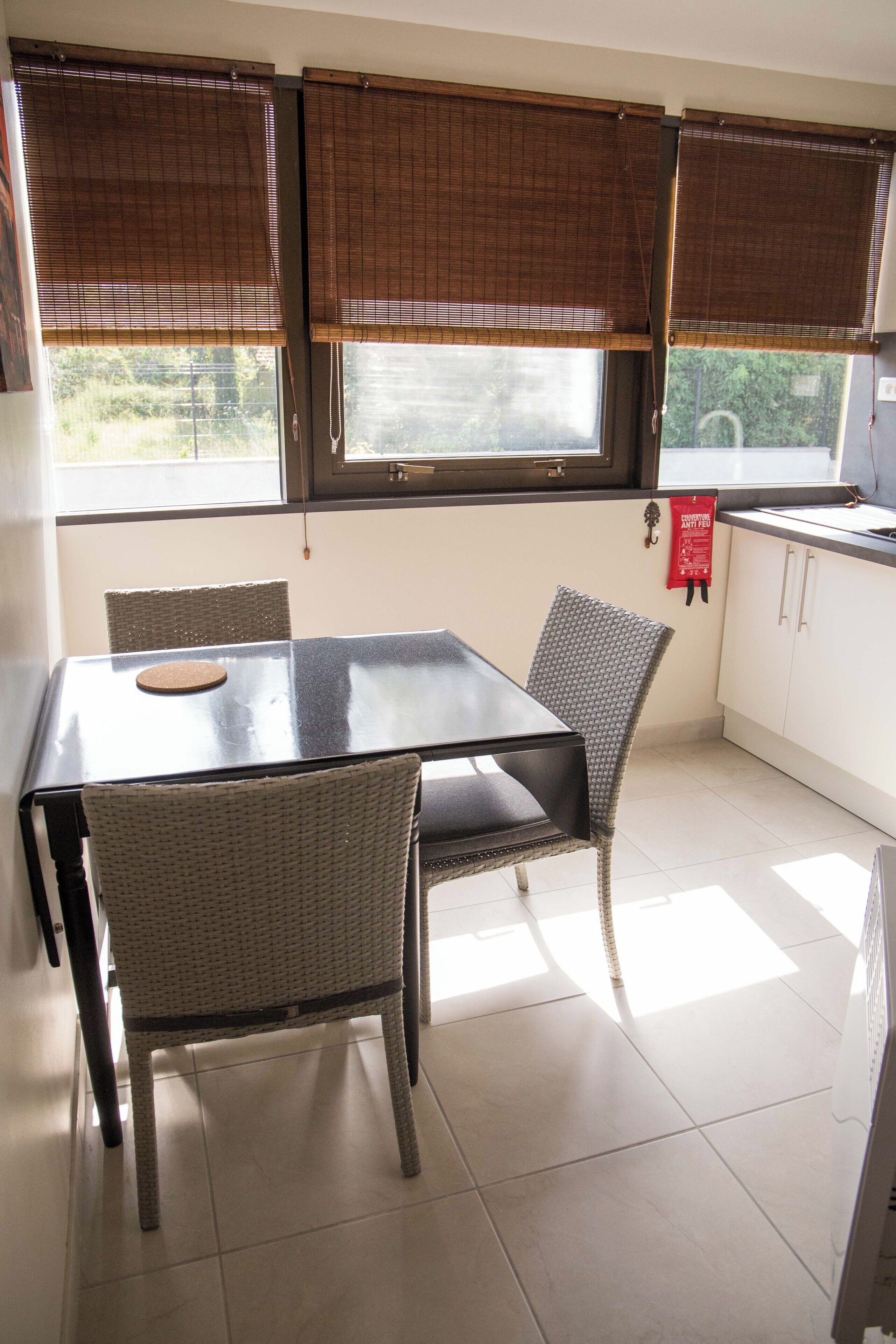 A dining area with a table and chairs, a window with blinds, and a kitchen area with cabinets.