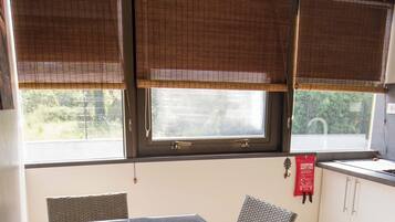 A dining area with a table and chairs, a window with blinds, and a kitchen area with cabinets.