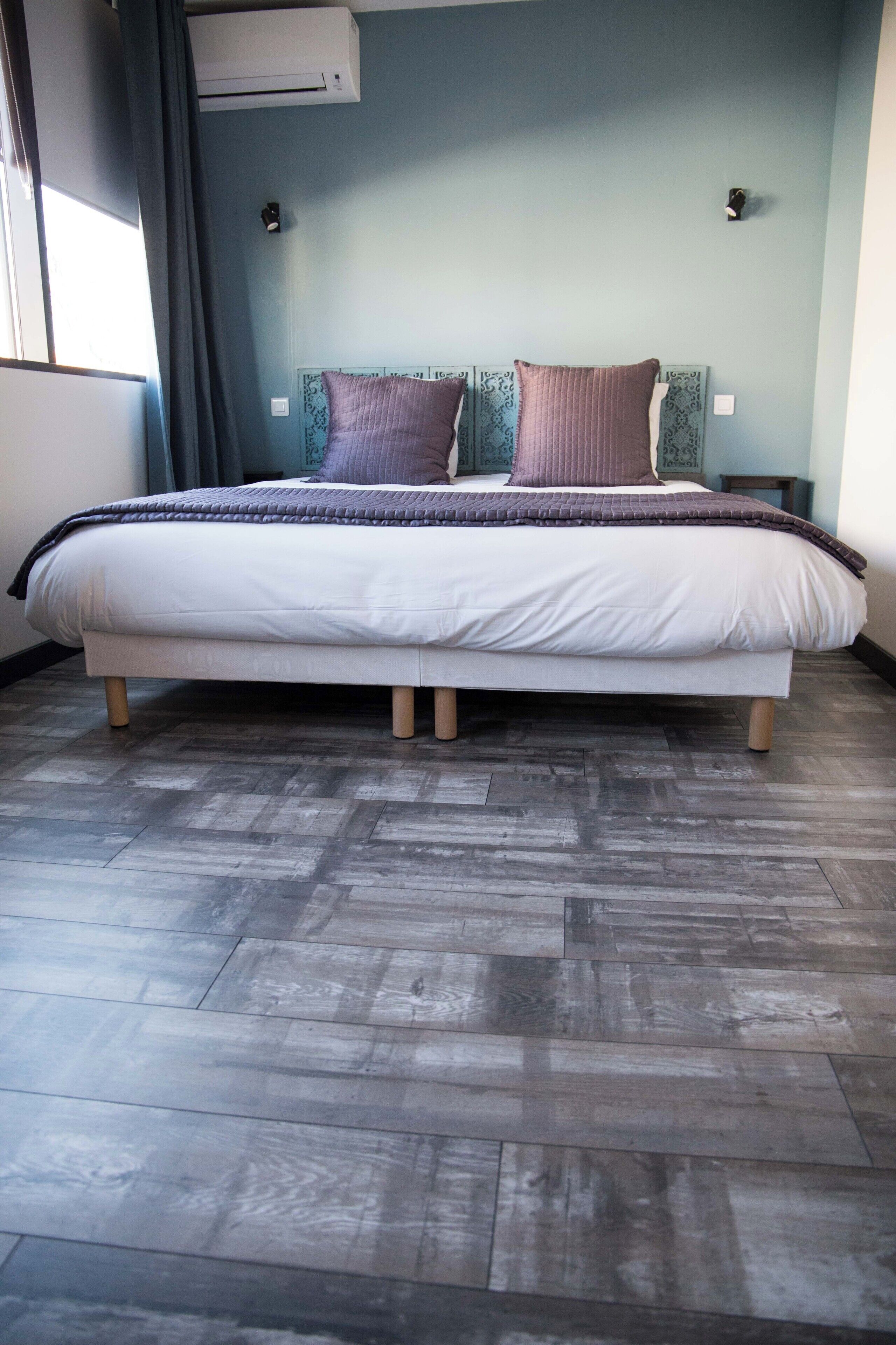 A neatly made bed with a patterned headboard, a dark wooden floor, and a wall-mounted air conditioner.