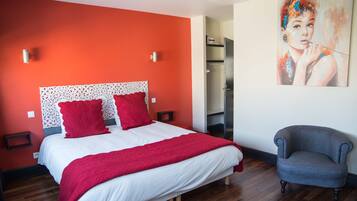 A bedroom with a bed, red pillows, a grey armchair, and a painting on the wall.