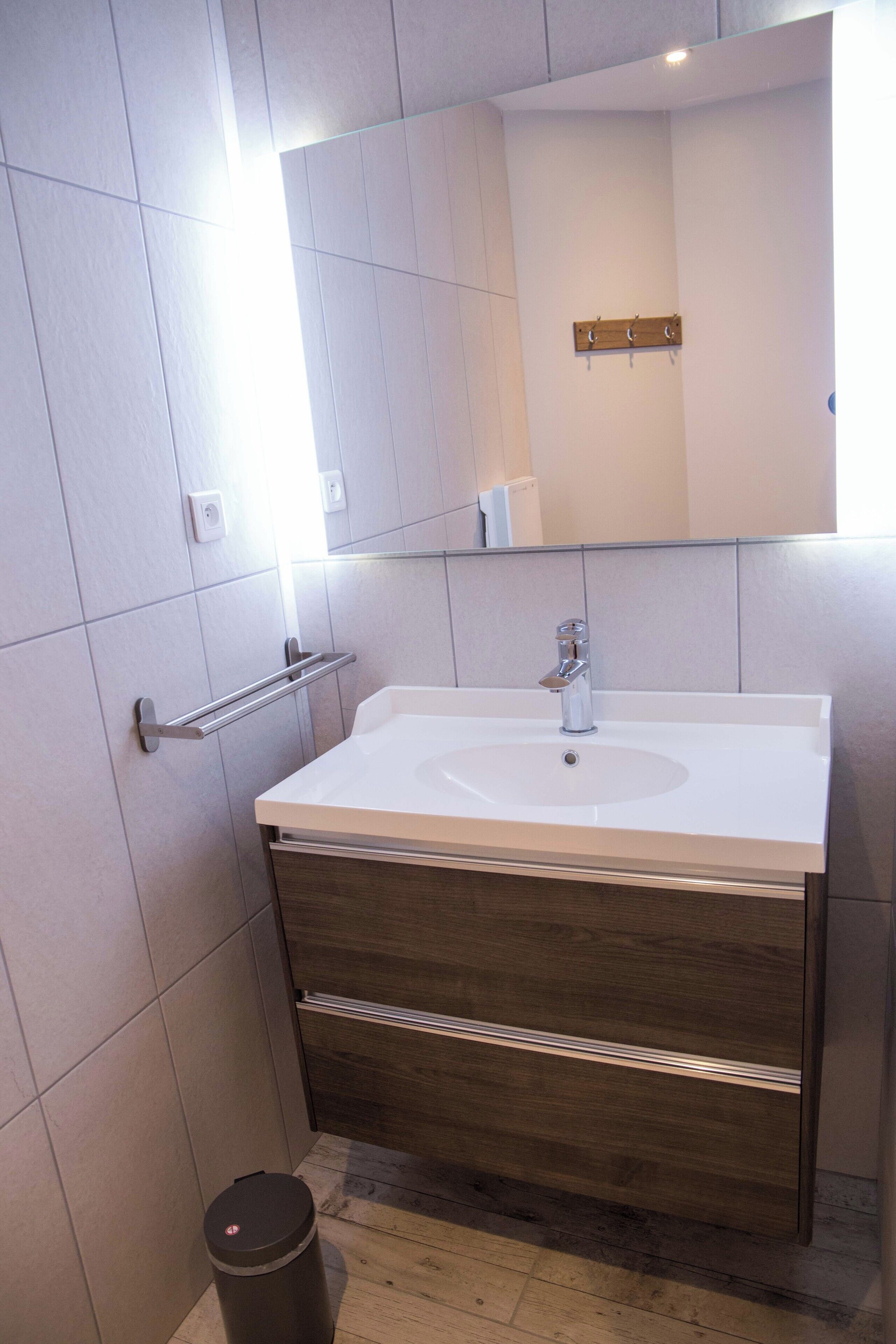 A bathroom with a white sink, wooden vanity, and a mirror above the sink.
