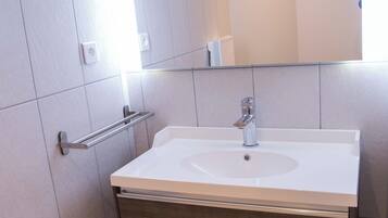 A bathroom with a white sink, wooden vanity, and a mirror above the sink.
