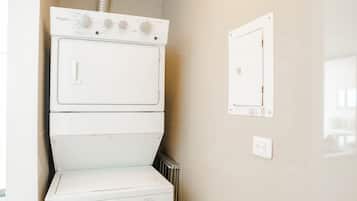 Una lavadora y secadora apiladas en un cuarto de lavado, con una etiqueta de eficiencia energética visible y un enchufe eléctrico en la pared.