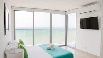 A hotel room with a bed, a TV, and a balcony with a view of the sea.