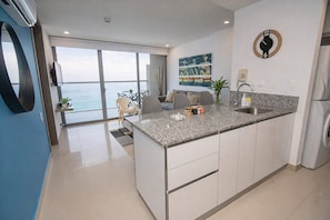 Een moderne keuken met een granieten aanrecht, een ingebouwd spoelbakje en uitzicht op de oceaan door grote ramen.