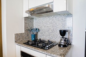 Une cuisine dotée d’un plan de travail en granit, d’une cuisinière à gaz, d’une machine à café et d’un porte-ustensiles bleu.