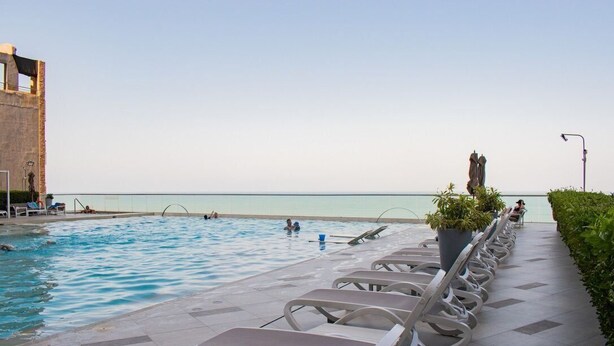 A pool area with lounge chairs and a view of the sea.