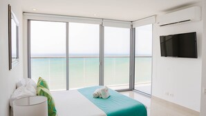 A hotel room with a bed, a TV, and a balcony with a view of the sea.