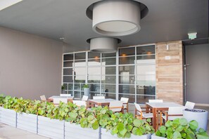 Un espace extérieur aménagé avec des tables et des chaises, un jardinier avec des plantes vertes et un design de plafond moderne.