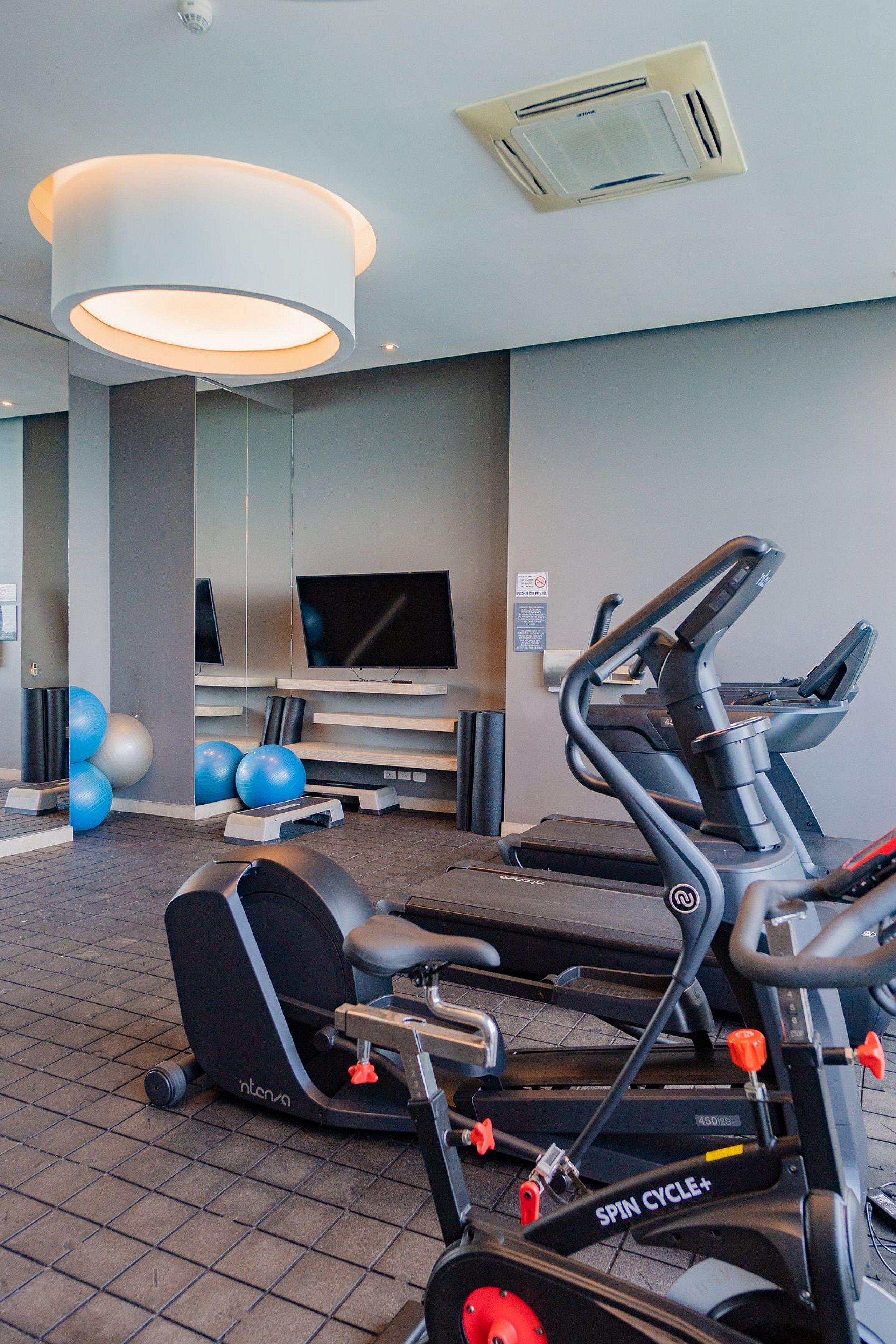 Ein Fitnessstudio mit Laufbändern, Gymbällen und einem Fernseher an der Wand.