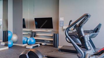 Une salle de sport équipée de tapis de course, de ballons d’exercice et d’un téléviseur fixé au mur.