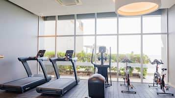 A gym with treadmills, an elliptical, and a stationary bike, large windows, and a tiled floor.