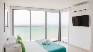 A hotel room with a bed, a TV, and a balcony with a view of the sea.