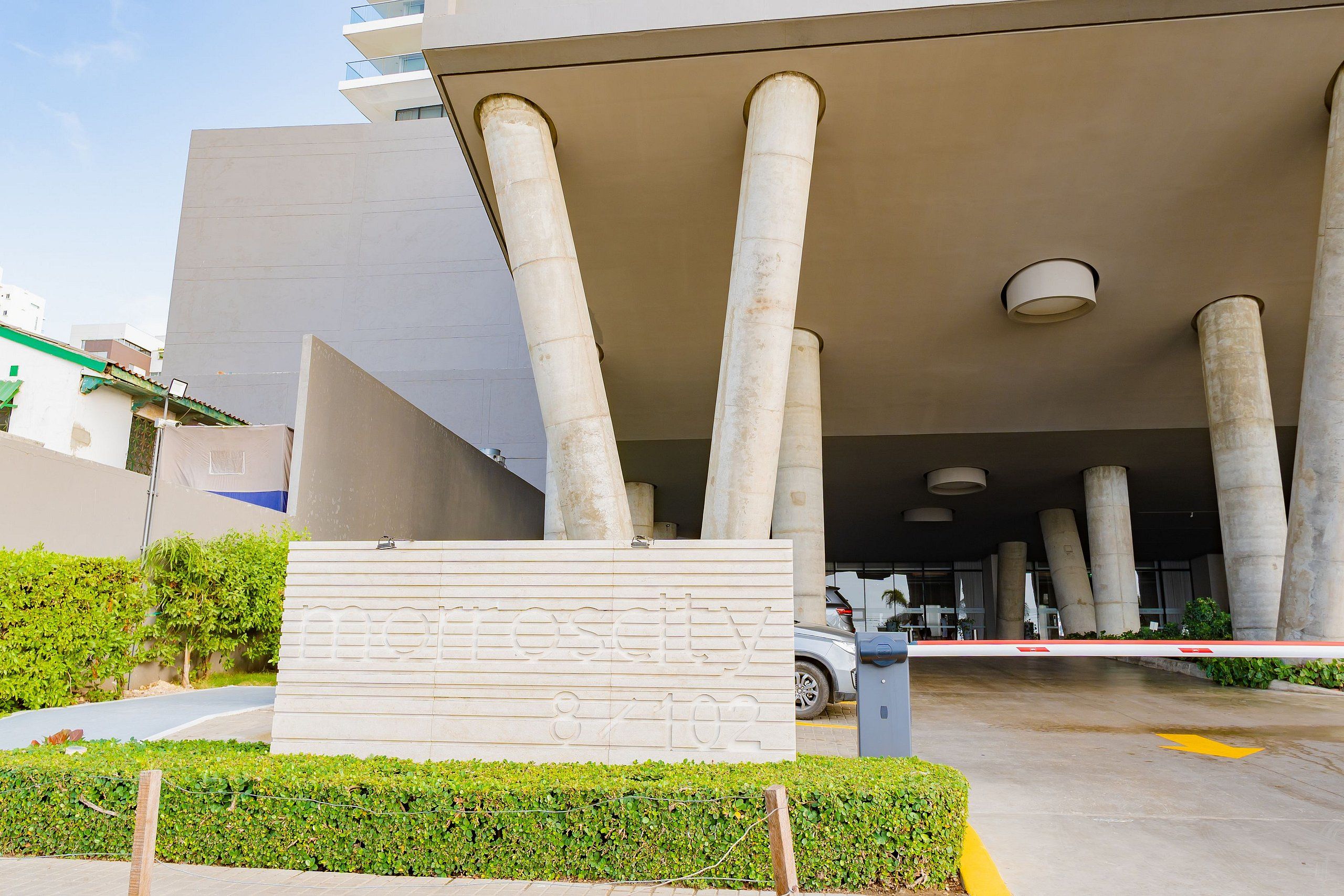 A modern building entrance with large concrete columns, a gated driveway, and a sign with numbers.