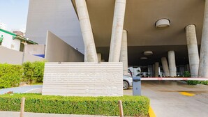 A modern building entrance with large concrete columns, a gated driveway, and a sign with numbers.