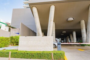 Una entrada moderna con grandes columnas de hormigón, un camino de acceso con portones y un letrero con números.