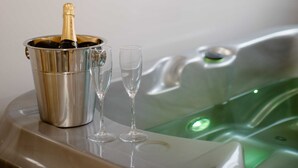 Une bouteille de champagne dans un seau en métal, accompagnée de deux verres posés sur une surface réfléchissante, une carte encadrée accrochée au mur et un jacuzzi éclairé de lumière verte.