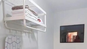 Un salon moderne avec un téléviseur à écran plat posé sur un meuble blanc, une étagère murale ornée d’une serviette à motifs géométriques et un tableau encadré au-dessus du téléviseur.