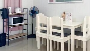 Une petite pièce propre, avec une table et des chaises blanches, un four à micro-ondes, un ventilateur et un miroir au mur.