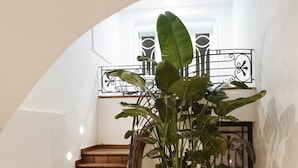Una escalera con una planta en maceta, paredes blancas y barandilla de metal.