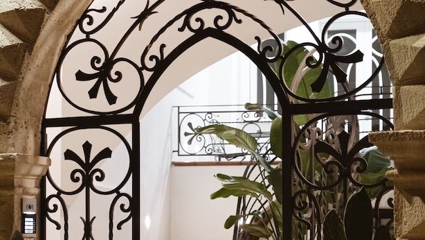 Un arco con detalles de metal ornamentado, una escalera y macetas con plantas.