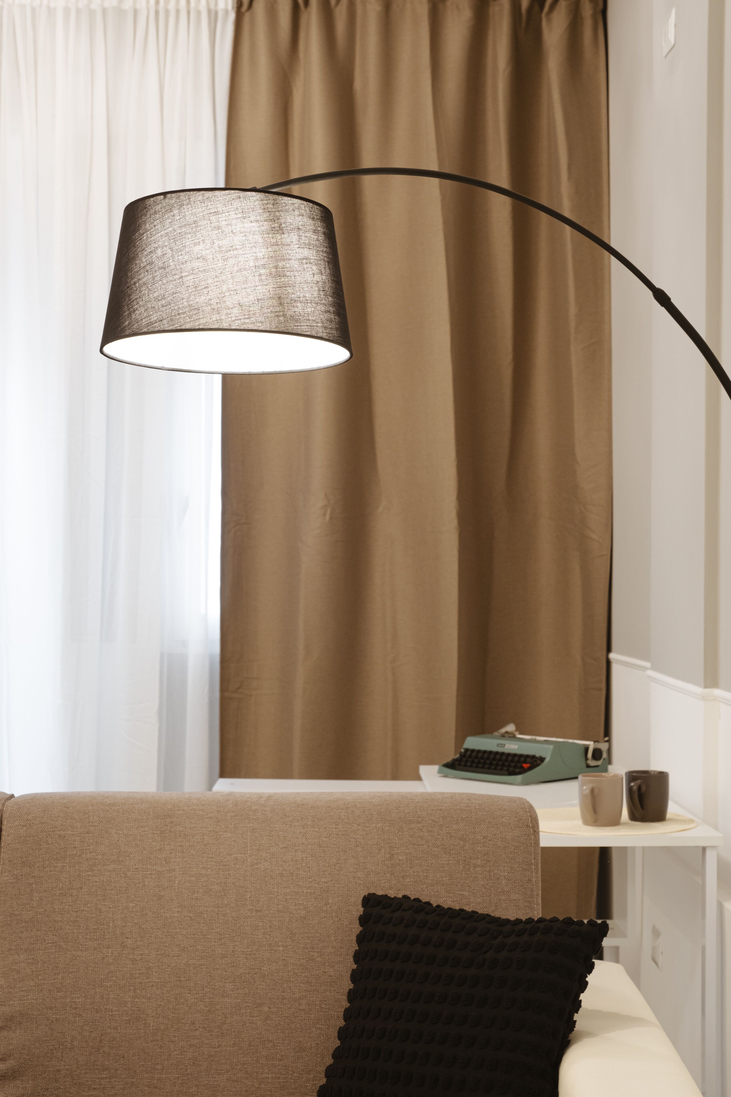 Una habitación con un sofá, una lámpara, una máquina de escribir y una taza sobre una mesita.