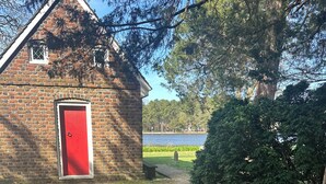 A brick building with a red door, a paved pathway, a bench, and a view of a lake. - Farmhouse Charm Woolford Studio Apt. w/ Amazing Eastern Shore Sunrise & Sunsets
 (Woolford)