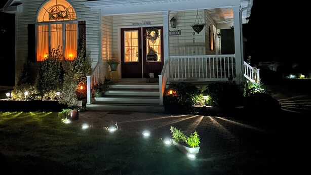 A two-story house with a porch, a welcome sign, and a well-lit front yard. - Farmhouse Charm Woolford Studio Apt. w/ Amazing Eastern Shore Sunrise & Sunsets
 (Woolford)