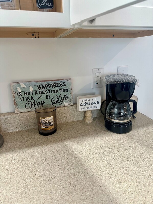 A kitchen counter with a coffee maker, a candle, and a motivational sign. - Farmhouse Charm Woolford Studio Apt. w/ Amazing Eastern Shore Sunrise & Sunsets
(Woolford)
