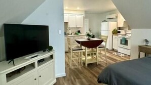 A bedroom with a bed, a TV on a stand, and a kitchenette in the background. - Farmhouse Charm Woolford Studio Apt. w/ Amazing Eastern Shore Sunrise & Sunsets
 (Woolford)