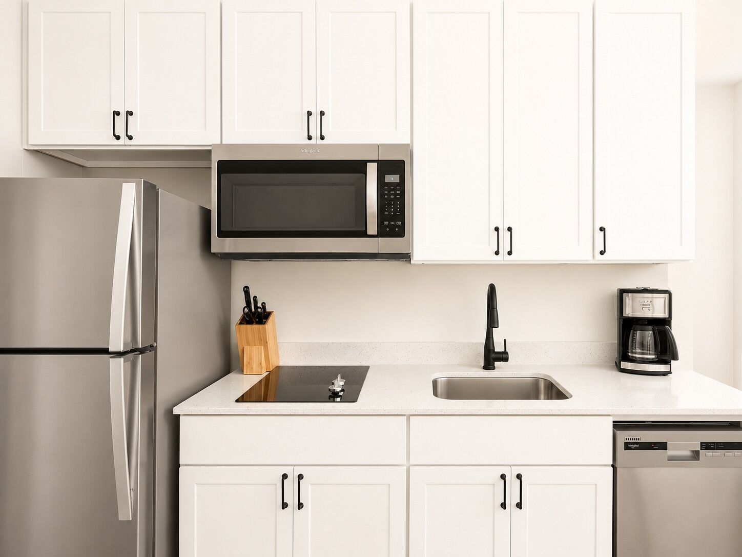 A modern kitchen with white cabinets, a stainless steel refrigerator, a microwave, a coffee maker, and a dishwasher.