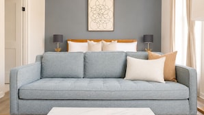 Un salon moderne avec un canapé gris, une table basse blanche et une œuvre d’art abstraite accrochée au mur.