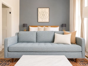 Ein modernes Wohnzimmer mit einem grauen Sofa, einem weißen Couchtisch und einem an der Wand hängenden abstrakten Kunstwerk.