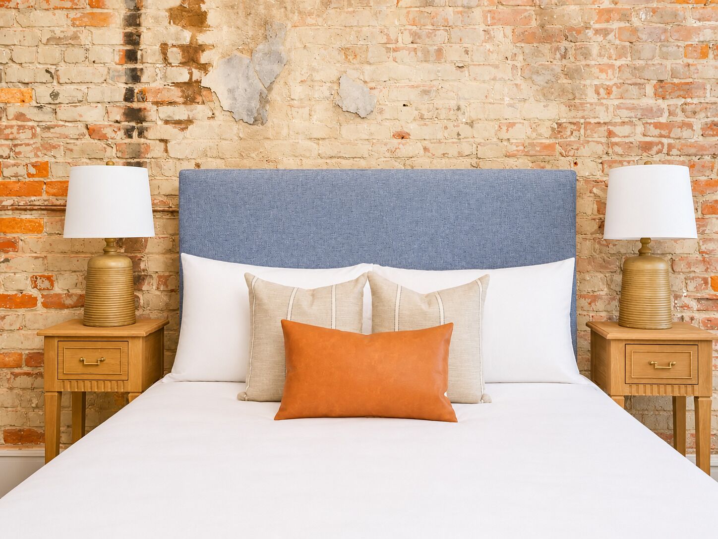 A bed with a blue headboard, two bedside tables with lamps, and a brick wall background.
