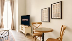 Une pièce comprenant une télévision, deux tableaux encadrés, une table à manger avec des chaises, un meuble en bois et un tapis à motifs.